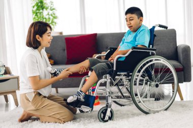 Asyalı fizyoterapistin portresi engelli çocuk sağlığı sorununa rehabilitasyon kliniğinde tekerlekli sandalyede oturarak yardım ve oyun oynayarak yardımcı oluyor.