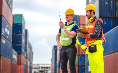 Miğferli iki mühendis konteynırı ustabaşı ayakta çalışıyor ve telsiz kullanarak stokları yükleme için konteynıra koyuyor. Lojistik ve iş ihracatı