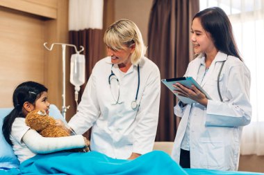 Gülümseyen kadın doktor servisi, küçük kız hastayla konuşma ve danışma konuşmalarını destekliyor. Oyuncak ayıyı ver ve hastanede bilgileri kontrol et.