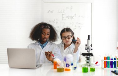 Okuldaki deney laboratuarında test tüpünde sıvı karıştırırken ve analiz ederken araştırma yapmayı öğrenen ve kimyasal deney yapan bir grup küçük sevimli öğrenci. Eğitim.