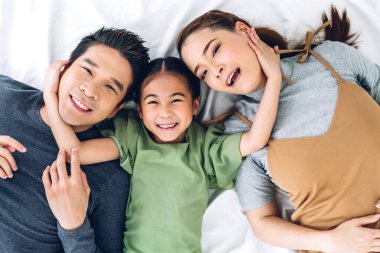 Portrenin en üst görüntüsü mutlu bir şekilde gülümseyen Asyalı bir aile babası ve annesi ve genç bir ebeveyni olan küçük Asyalı bir kız kameraya bakıyor.