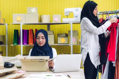 Gülümseyen iki güzel Müslüman kadının portresi Asyalı serbest çalışan bir kadın dizüstü bilgisayarla online alışveriş yapıyor evdeki paket kutusuyla iş yeri çevrimiçi nakliyat ve teslimat.