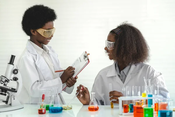 Two african american cute little boy and girl student child learning research and doing a chemical experiment while making analyzing and mixing liquid in test tube at science class on the table.Education and science concept