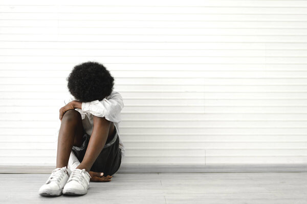 Portrait of sad depressed black african american cute little boy child alone sitting on floor at home
