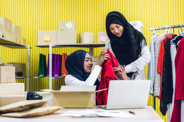Gülümseyen iki güzel Müslüman kadının portresi Asyalı serbest çalışan bir kadın dizüstü bilgisayarla online alışveriş yapıyor evdeki paket kutusuyla iş yeri çevrimiçi nakliyat ve teslimat.