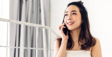 Mutlu, neşeli, güzel Asyalı bir kadının gülümsemesi modern akıllı telefon teknolojisine bakarak rahatlıyor. Düşen bir kız telefonuyla eğleniyor ve evdeki teknolojinin üzerine mesaj yazıyor.