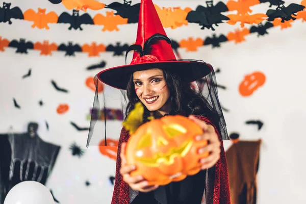 Cadılar bayramı partisinde balkabağı tutan ve Cadılar Bayramı kostümleri giyip arka planda yarasalar ve balonlarla poz veren bir kadın. Cadılar Bayramı bayramı kutlaması konsepti.