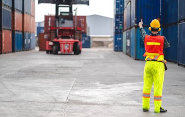 Miğferli profesyonel mühendis konteynır ustabaşı ayakta çalışıyor ve telsiz kullanıyor stokları yükleme için konteynıra koyuyor. Lojistik ve iş ihracatı