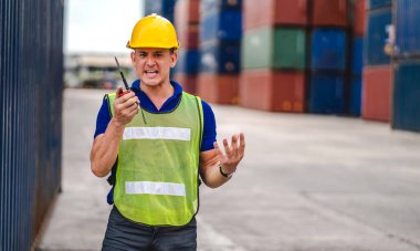 Miğferli profesyonel mühendis konteynır ustabaşı ayakta çalışıyor ve telsiz kullanıyor stokları yükleme için konteynıra koyuyor. Lojistik ve iş ihracatı