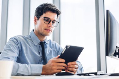 Sandalyeye otururken tablet bilgisayar teknolojisine bakan yakışıklı, kendine güvenen iş adamı. İş günlerinde iş arkadaşları yöneticileri iş yerinde bir fincan kahveyle birlikte iş adamları.