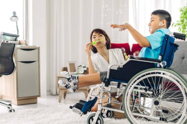 Asyalı fizyoterapistin portresi engelli çocuk sağlığı sorununa rehabilitasyon kliniğinde tekerlekli sandalyede oturarak yardım ve oyun oynayarak yardımcı oluyor.