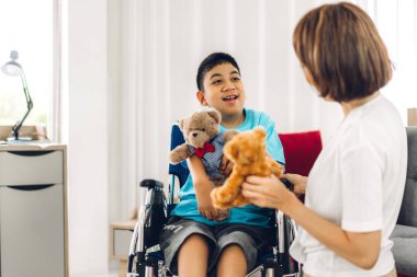 Asyalı fizyoterapistin portresi engelli çocuk sağlığı sorununa rehabilitasyon kliniğinde tekerlekli sandalyede oturarak yardım ve oyun oynayarak yardımcı oluyor.