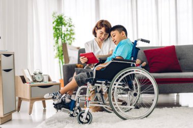 Asyalı fizyoterapistin portresi engelli çocuk sağlığı sorununa rehabilitasyon kliniğinde tekerlekli sandalyede oturarak yardım ve oyun oynayarak yardımcı oluyor.
