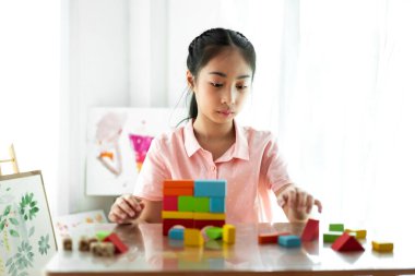 Küçük tatlı kız evde tahta blok oyuncakları oynarken eğleniyor.