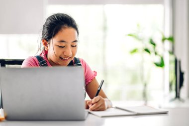 Okul çocuğu küçük kız öğreniyor ve dizüstü bilgisayara bakıyor ev ödevi yapıyor çevrimiçi eğitim sistemi ile bilgi öğreniyor. Evde öğretmenle çocuk video konferansı