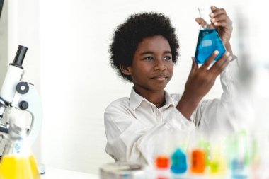 Afrika kökenli, sevimli, küçük bir çocuk. Araştırma yapmayı öğreniyor ve kimyasal bir deney yapıyor. Fen bilimleri sınıfında sıvıyı analiz edip karıştırıyor.