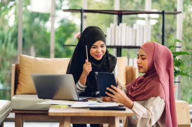 Genç, gülümseyen mutlu Asyalı Müslüman kadın evde dizüstü bilgisayar, tablet çalışma ve video konferans kullanarak rahatlıyor. Ev konseptinden iş.