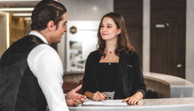 Genç yakışıklı işadamı konuşuyor ve kayıt bilgilerini lobideki otel resepsiyonunda duran bayan resepsiyonistle kontrol ediyor. Modern otel lobisinde. 
