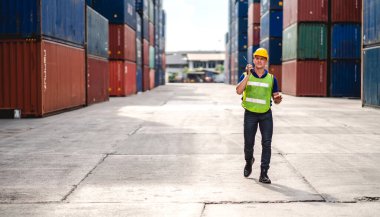 Miğferli profesyonel mühendis konteynır ustabaşı ayakta çalışıyor ve telsiz kullanıyor stokları yükleme için konteynıra koyuyor. Lojistik ve iş ihracatı