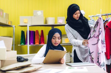 Gülümseyen iki güzel Müslüman kadının portresi Asyalı serbest çalışan bir kadın dizüstü bilgisayarla online alışveriş yapıyor evdeki paket kutusuyla iş yeri çevrimiçi nakliyat ve teslimat.