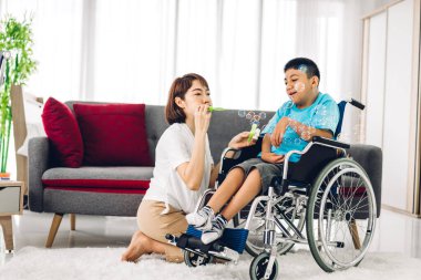 Mutlu aşk portresi. Asyalı anne oynuyor ve bakıcı tekerlekli sandalyede oturan engelli çocuğa bakıyor. Evde engelli bakımı konseptinde iyi vakit geçiriyor.
