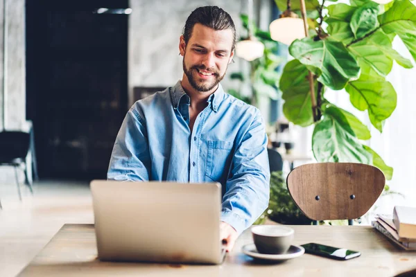 Yakışıklı sakallı hippi, kafeteryasında kahve olan dizüstü bilgisayarı kullanır ve ona bakar. İletişim ve teknoloji kavramı.