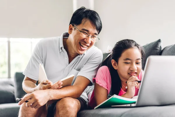 Father and asian kid little girl learning and looking at laptop computer making homework studying knowledge with online education e-learning system.children video conference with teacher tutor at home