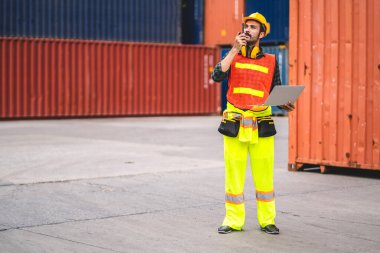 Miğferli profesyonel mühendis konteynır ustabaşı ayakta çalışıyor ve telsiz kullanıyor stokları yükleme için konteynıra koyuyor. Lojistik ve iş ihracatı