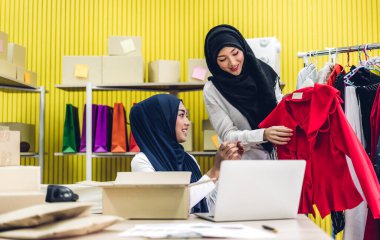 Gülümseyen iki güzel Müslüman kadının portresi Asyalı serbest çalışan bir kadın dizüstü bilgisayarla online alışveriş yapıyor evdeki paket kutusuyla iş yeri çevrimiçi nakliyat ve teslimat.