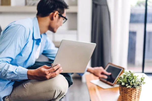 Young creative smiling happy asian man relaxing using laptop computer working and video conference meeting online chat at home.work from home concept