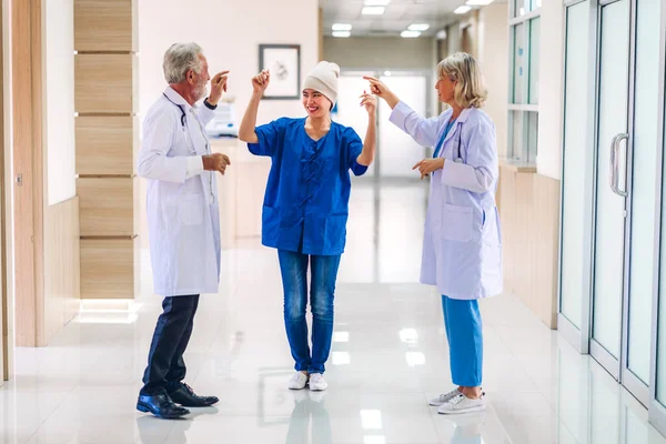 Professional medical doctor team with stethoscope in uniform discussing and dancing with happy patient woman with cancer cover head with headscarf of chemotherapy cancer in hospital.health care concept