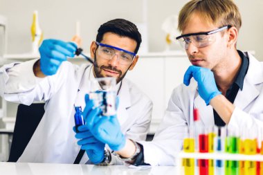 Profesyonel iki bilim adamı test tüpünde sıvı analiz ederken ve karıştırırken kimyasal bir deney yapıyor. Genç bilim adamı laboratuvarda cam üzerine kimyasal örnekler bırakıyor.