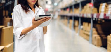 Gülümseyen Asyalı yönetici kadın portresi ayakta duruyor ve malzeme ve gereçleri depoda kontrol etmek için tablet bilgisayardan ayrıntılı talimat veriyor. Lojistik ve iş ihracatı
