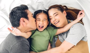 Portrenin en üst görüntüsü mutlu bir şekilde gülümseyen Asyalı bir aile babası ve annesi ve genç bir ebeveyni olan küçük Asyalı bir kız kameraya bakıyor.