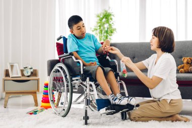Asyalı fizyoterapistin portresi engelli çocuk sağlığı sorununa rehabilitasyon kliniğinde tekerlekli sandalyede oturarak yardım ve oyun oynayarak yardımcı oluyor.