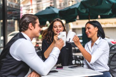 Bir grup neşeli genç arkadaş buluşmayı tartışıyor ve birlikte kahve içerek eğleniyorlar. Kafe masasında ve restoranda karışık ırkçı insanlar oturuyor.