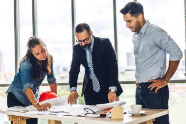 İnşaat alanındaki masanın üzerinde tasarım ve inşaat araçlarıyla çalışan miğferli kargo ustabaşıları.