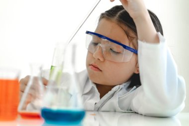 Şirin küçük kız öğrenci araştırma yapmayı ve kimyasal deney yapmayı öğrenirken fen bilimleri sınıfında sıvıyı analiz edip karıştırıyor. Eğitim ve bilim konsepti.