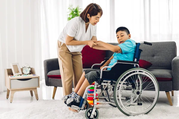 Asyalı fizyoterapistin portresi engelli çocuk sağlığı sorununa rehabilitasyon kliniğinde tekerlekli sandalyede oturarak yardım ve oyun oynayarak yardımcı oluyor.