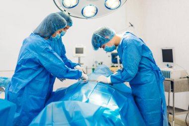 Profesyonel anestezi uzmanı doktor tıp ekibi ve asistanı modern hastane acil servisinde cerrahi ekipmanla jinekolojik ameliyata hazırlanıyor.
