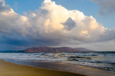 Yaktı yükselen güneş, mavi dalgalar, kahverengi kum ve kırmızı hill tarafından deniz üzerinde büyük bulut