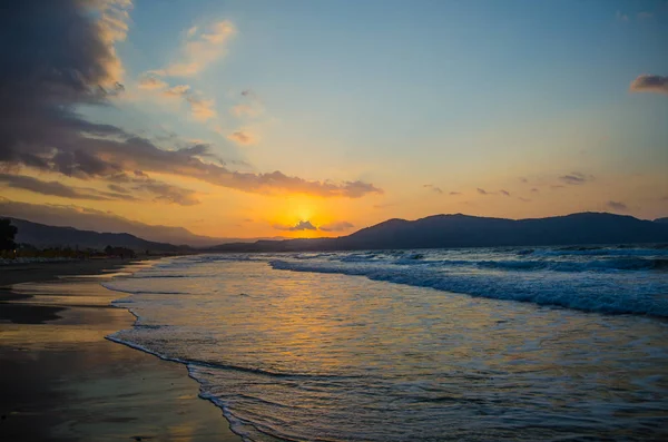 Sunset over the sea, the rolling calm waves, sandy beach. Skay orange-blue  light cloud.