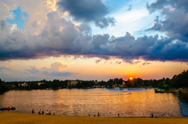 Tatilciler ile şehir gölünün kıyısında batan güneş ve sarı kum bir şerit ile Akşam gökyüzü.