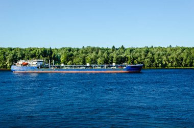 Mavi suyla nehirde yüzen mavna. Yeşil yeşillik ve huş dalları ile yüksek çimenli Banka dan görünümü.