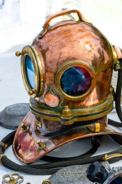 Hafif bir arka plan üzerinde diğer aksesuarları ile sergi masası üzerinde yatan ağır bakır dalış kask