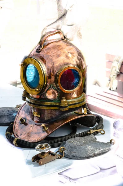 Heavy copper diving helmet lying on the exhibition table with other accessories on a light background