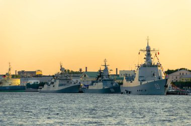 Gün batımı gökyüzüne karşı geniş bir nehrin sularında demirlemiş üç modern savaş gemisi