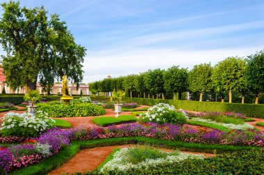 18. yüzyılda inşa edilen Monplaisir, Peterhof 'un mavi gökyüzüne karşı yeşil ağaçlar, çalılar ve çiçeklerle çevrili kırmızı bir çatısı var..