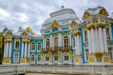 Mavi bir Barok köşkünün bir parçası. Arka planda beyaz sütunlar var. Mavi bir gökyüzünün arka planında sonbahar ağaçları.
