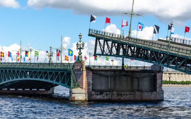 Köprünün kemerlerini indiriyorum, bayramın onuruna renkli bayraklarla süslenmiş mavi gökyüzü ve bulutların arka planına karşı